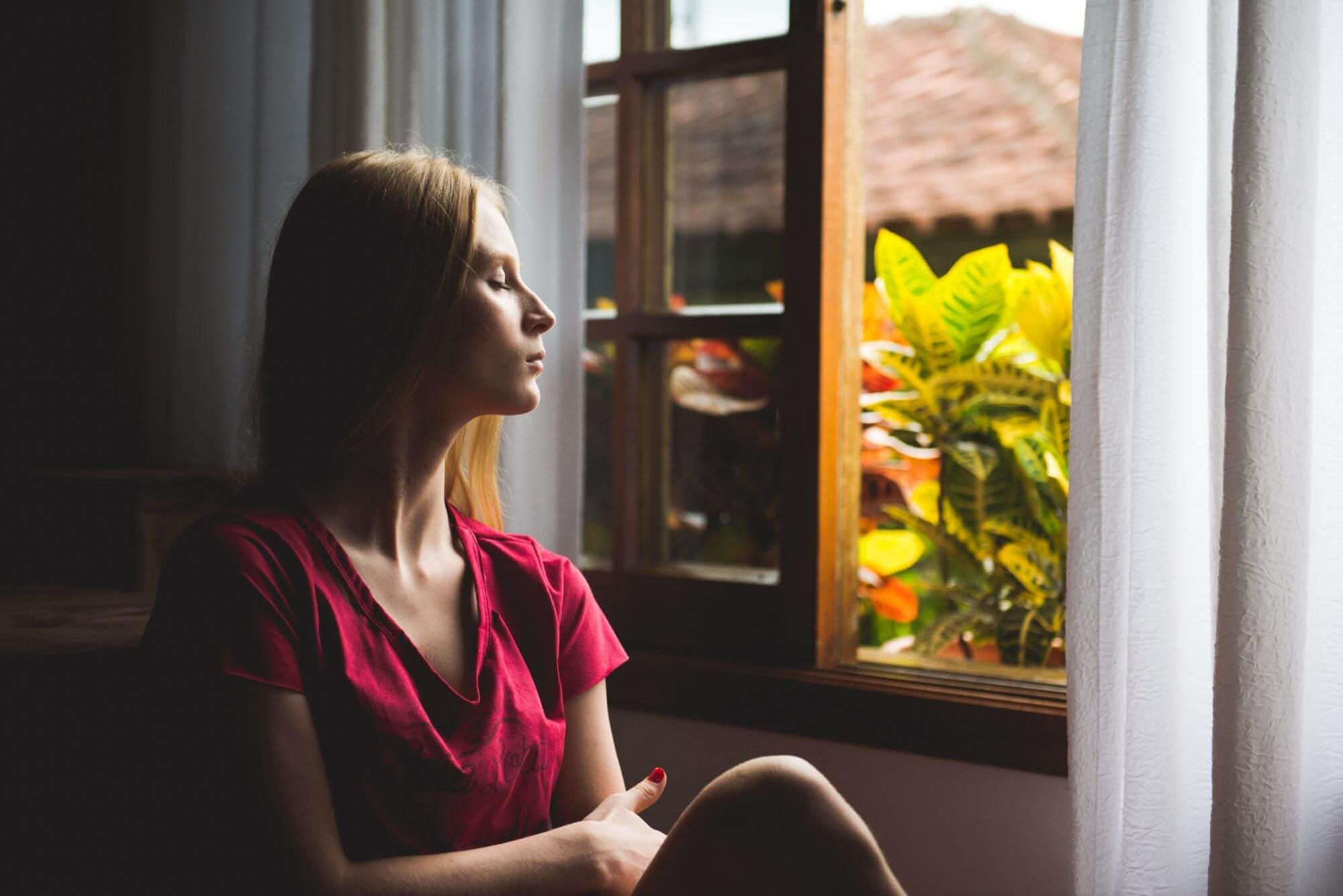 Femme qui se détend et respire profondément devant sa fenêtre ouverte